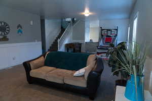 Living room with stairs, carpet, wainscoting, and a decorative wall