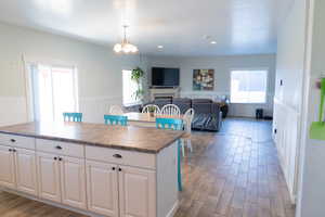 Kitchen with light wood-type flooring, wainscoting, white cabinetry, healthy amount of natural light, and hanging light fixtures
