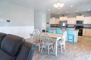 Dining space with a wainscoted wall, light wood-type flooring, a decorative wall, recessed lighting, and a chandelier