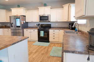 Kitchen featuring stainless steel appliances, white cabinets, light wood finished floors, and dark countertops
