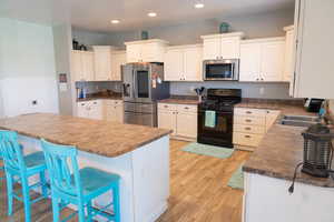 Kitchen with appliances with stainless steel finishes, a breakfast bar area, white cabinetry, light wood finished floors, and recessed lighting