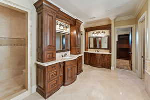 Bathroom with crown molding, two vanities, tiled shower, and tile patterned floors