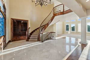 Entryway with decorative columns, marble tiled floors, a chandelier, a towering ceiling, and stairs