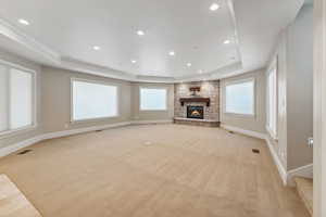 Unfurnished living room featuring light carpet, a tray ceiling, a fireplace, recessed lighting, and crown molding