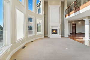 Unfurnished living room with ornate columns, a glass covered fireplace, light carpet, a high ceiling, and light wood-style floors