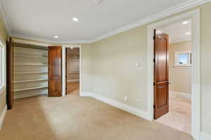 Unfurnished bedroom with a spacious closet, light colored carpet, crown molding, and recessed lighting