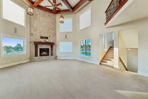 Unfurnished living room featuring coffered ceiling, beam ceiling, a stone fireplace, a ceiling fan, and carpet flooring