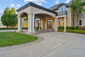 View of exterior entry featuring french doors, a balcony, a yard, stucco siding, and stone siding