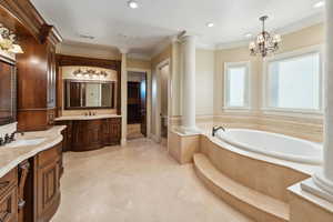 Full bath featuring decorative columns, crown molding, two vanities, a garden tub, and recessed lighting