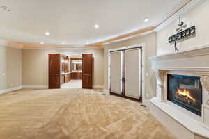Unfurnished living room featuring light carpet, ornamental molding, a high end fireplace, recessed lighting, and french doors