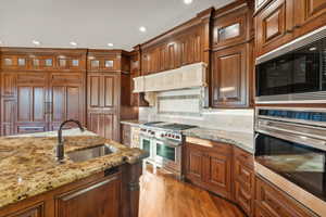 Kitchen with stainless steel appliances, wood finished floors, recessed lighting, brown cabinets, and glass insert cabinets