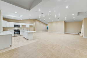 Kitchen featuring a center island, recessed lighting, appliances with stainless steel finishes, white cabinetry, and vaulted ceiling