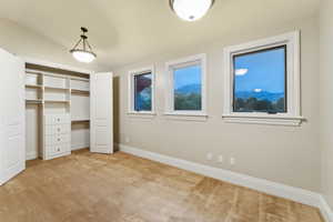 Unfurnished bedroom featuring light colored carpet, vaulted ceiling, a closet, and a mountain view