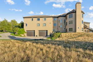 Rear view of property with an attached garage, driveway, stucco siding, and a chimney