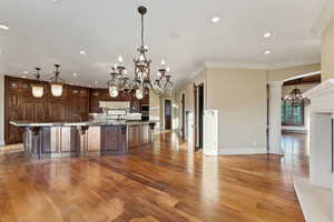 Kitchen featuring a chandelier, recessed lighting, crown molding, hardwood / wood-style floors, and a kitchen bar