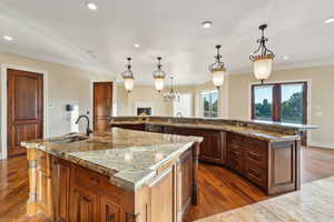 Kitchen featuring dark wood-type flooring, crown molding, a center island with sink, a warm lit fireplace, and a breakfast bar area