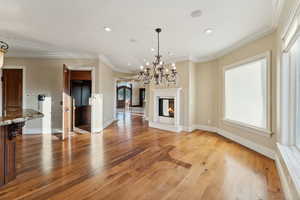 Unfurnished living room featuring light wood-style flooring, ornamental molding, a chandelier, a glass covered fireplace, and recessed lighting