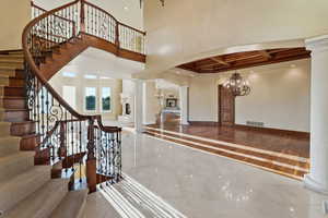 Entrance foyer with a chandelier, decorative columns, arched walkways, stairway, and marble finish floors