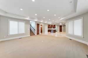 Unfurnished living room with light carpet, ornamental molding, recessed lighting, stairway, and a tray ceiling