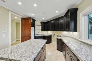 Kitchen with ornamental molding, recessed lighting, light stone counters, and a center island