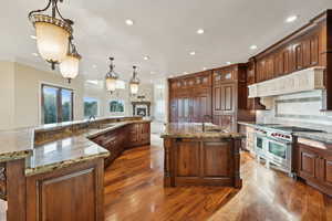 Kitchen with a spacious island, dark wood-style floors, double oven range, backsplash, and light stone countertops