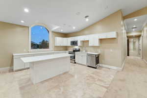 Kitchen featuring vaulted ceiling, a kitchen island, appliances with stainless steel finishes, recessed lighting, and white cabinetry