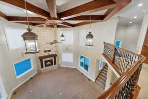 Carpeted living room with a ceiling fan, a towering ceiling, recessed lighting, a stone fireplace, and beam ceiling