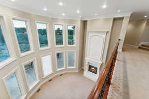 Unfurnished living room with light carpet, ornamental molding, recessed lighting, and a warm lit fireplace