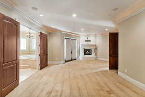 Unfurnished living room with a chandelier, light carpet, ornamental molding, a glass covered fireplace, and recessed lighting
