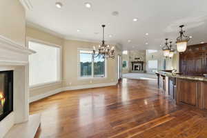 Kitchen with a high end fireplace, open floor plan, ornamental molding, wood finished floors, and a chandelier