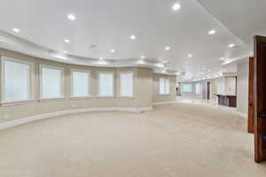 Unfurnished living room with light carpet, crown molding, recessed lighting, and a raised ceiling