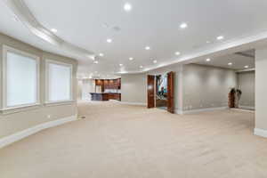 Unfurnished living room featuring light colored carpet, crown molding, recessed lighting, bar, and a raised ceiling