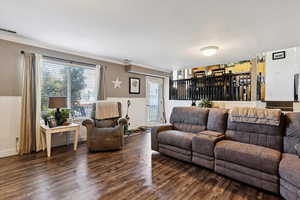 Living area featuring wainscoting, dark wood-style floors, crown molding, and a textured ceiling