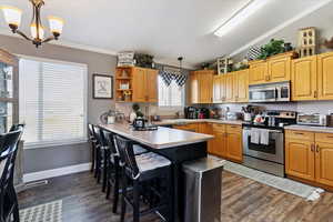 Kitchen featuring appliances with stainless steel finishes, ornamental molding, vaulted ceiling, dark wood finished floors, and a breakfast bar