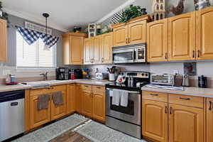 Kitchen featuring stainless steel appliances, crown molding, light countertops, wood finished floors, and pendant lighting