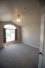 Carpeted spare room featuring lofted ceiling and baseboards