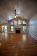 Unfurnished living room with a ceiling fan, wood finished floors, a fireplace, healthy amount of natural light, and vaulted ceiling