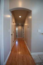 Corridor with arched walkways, light wood-type flooring, and recessed lighting
