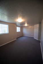 Unfurnished room with a textured ceiling and dark carpet