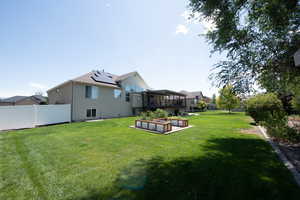 Rear view of property with a fenced backyard, roof mounted solar panels, and a vegetable garden