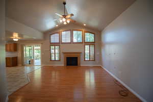 Unfurnished living room with ceiling fan, light wood-style flooring, a fireplace, and high vaulted ceiling