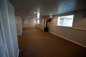 Below grade area with a wood stove, dark colored carpet, a textured ceiling, and recessed lighting