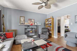 Living area featuring wood finished floors, ceiling fan, and radiator heating unit