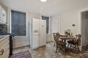 Kitchen featuring stone finish floors, white refrigerator with ice dispenser, gas range, white cabinets, and under cabinet range hood