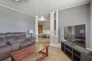 Living room featuring ornate columns, crown molding, and a wainscoted wall