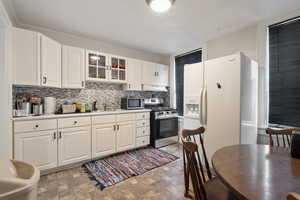 Kitchen with stainless steel appliances, decorative backsplash, stone finish flooring, light countertops, and white cabinetry