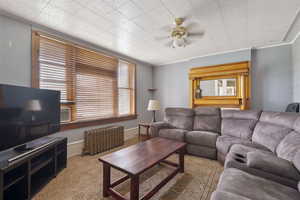 Living area with radiator, ornamental molding, carpet floors, and ceiling fan