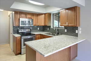 Kitchen featuring stainless steel appliances, a peninsula, decorative backsplash, brown cabinets, custom tile floors.