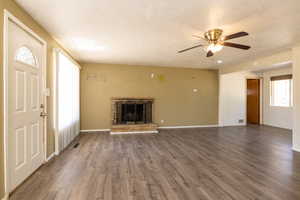 Unfurnished living room with a ceiling fan, wood finished floors, a brick fireplace, and a textured ceiling