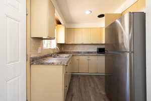 Kitchen with cream cabinetry, appliances with stainless steel finishes, dark wood-type flooring, tasteful backsplash, and dark countertops